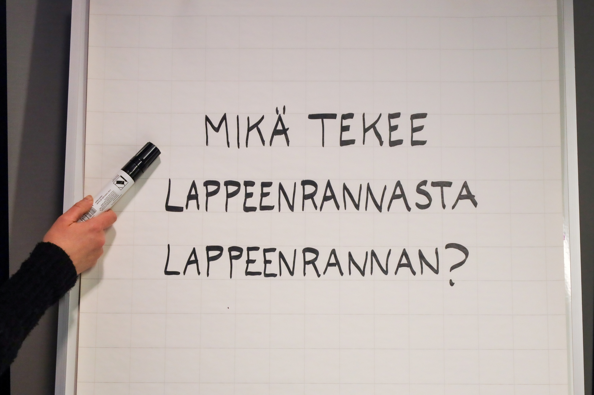 Fläppitaululla teksti "mikä tekee Lappeenrannasta Lappeenrannan?" ja käsi, joka osoittaa tekstiä tussilla.